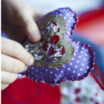 A child is learning to sew a heart on a piece of fabric using the Buttonbag Learn to Sew Suitcase Kit.