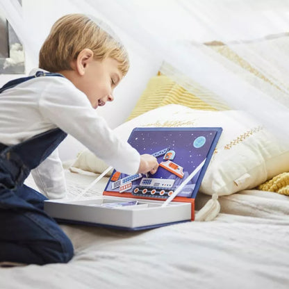 A young boy explores children's imagination while playing with the Janod Cosmos Magneti'book on a bed.