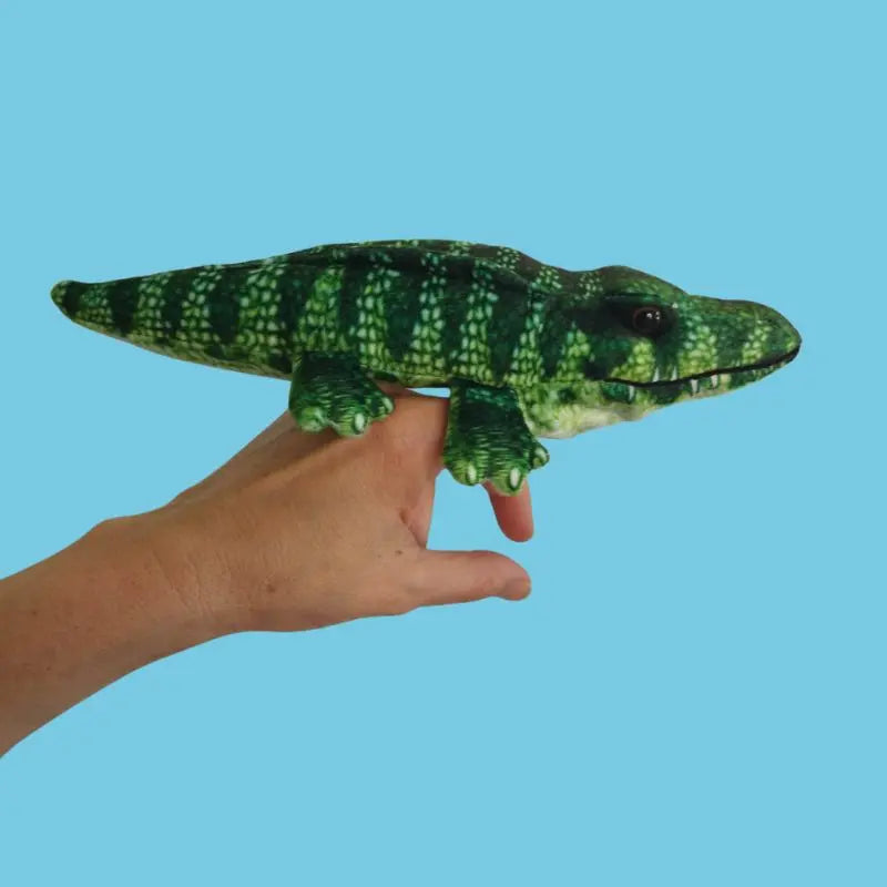A hand wears The Puppet Company Crocodile Finger Puppet – Little Creatures Range, its green and yellow design bright against a light blue background, ready for playful adventures.