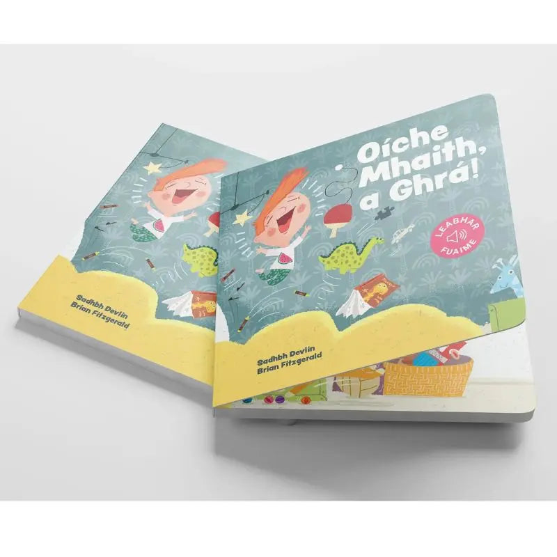 Two vibrant "Oíche Mhaith, a Ghrá" children's books are stacked on a white surface, each featuring an illustrated child and playful Irish-language bedtime story text on the cover.