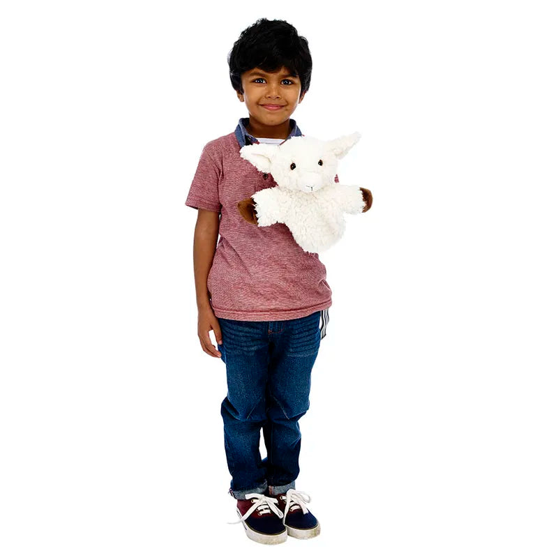 A young child smiles, holding The Puppet Company CarPets White Sheep hand puppet. Wearing a red shirt and blue jeans, the child stands against a plain white background—ideal for entertaining kids on long car journeys.