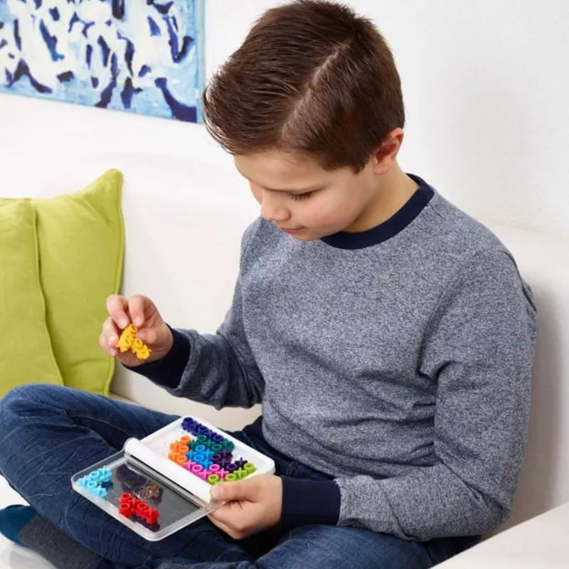 A young boy playing the game SmartGames IQ XOXO, facing challenges, on a couch.