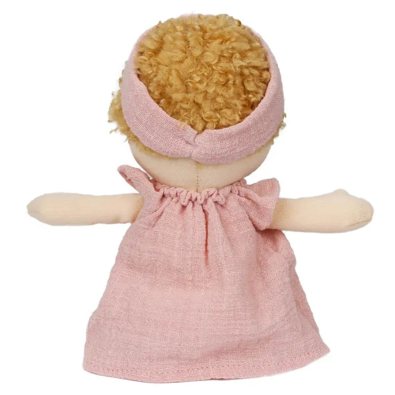 The Wilbery Baby Doll Girl Pink Outfit features curly blonde hair and a matching pink headband and dress, shown from the back with arms outstretched.