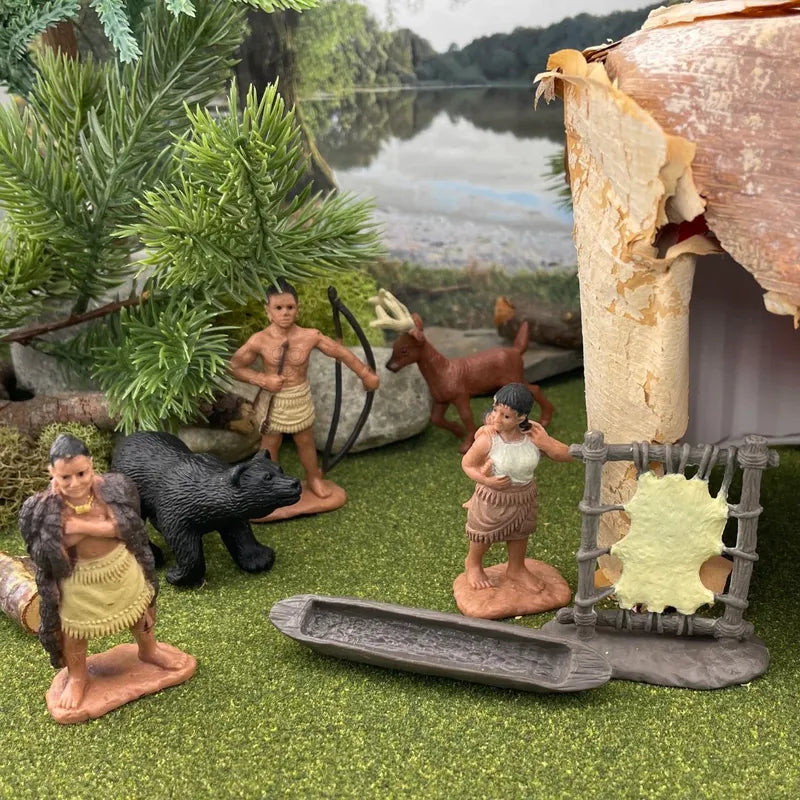 Miniature prehistoric scene with TOOB® Figurines Powhatan Indians, including a man, woman, and a child near a canoe, animals, and a hut, set against a backdrop featuring a serene lake