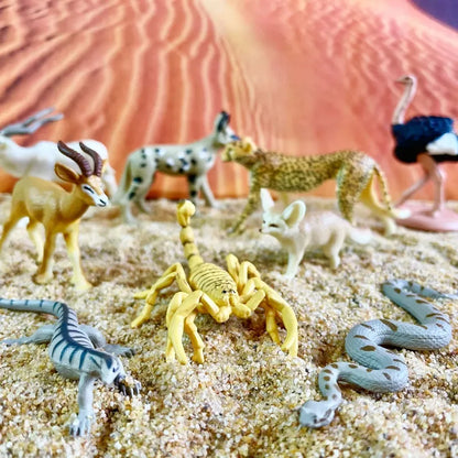 A collection of detailed miniature animal figures, including a scorpion, snakes, a leopard, and various other wildlife, displayed on a sandy surface against a blurred desert-like background. This set includes TOOB® Figurines Sahara Wüste educational toys.
