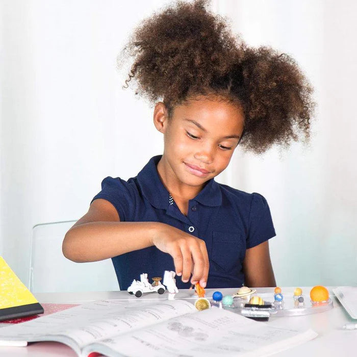 a young girl is playing with TOOBS® Figurines Space at a desk.