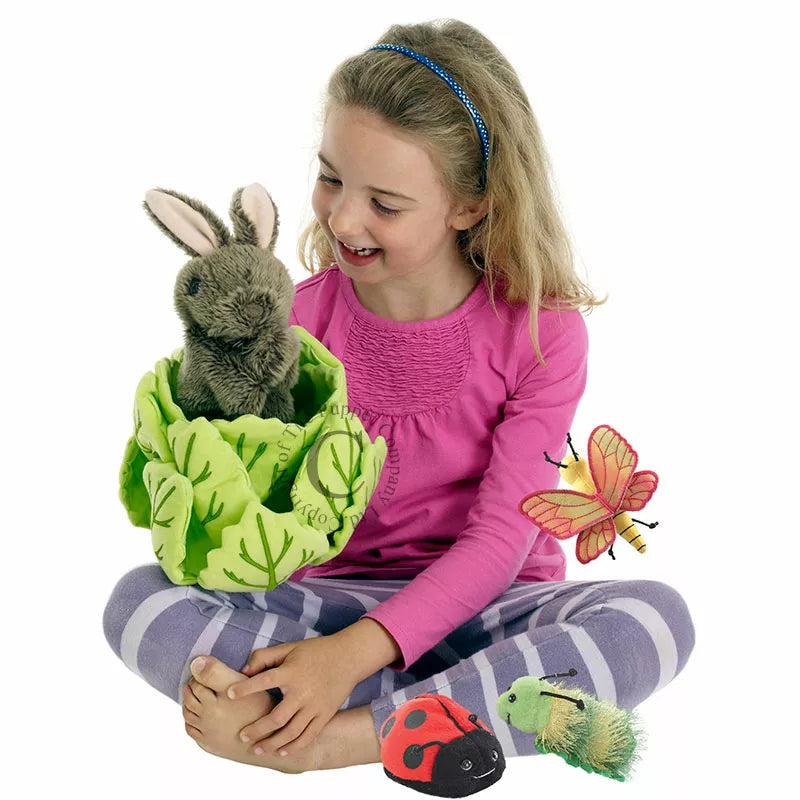 Smiling girl in a pink top and striped leggings holds a plush bunny in a leafy pouch, with toy ladybug, caterpillar, and butterfly nearby.