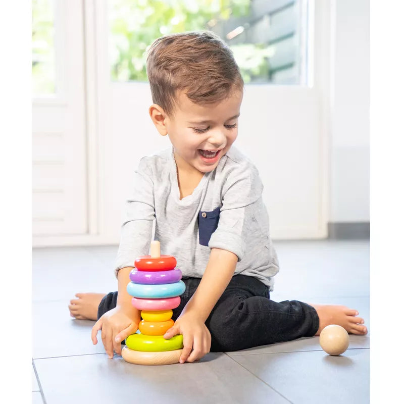 A young boy playing with the New Classic Toys Rainbow Stacking Toy on the floor, developing his fine-motor skills.