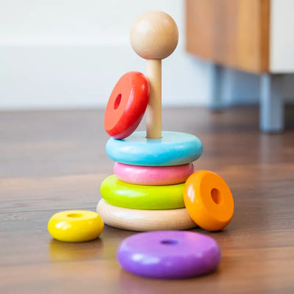 A stack of New Classic Toys Rainbow Stacking Toy on a wooden floor.