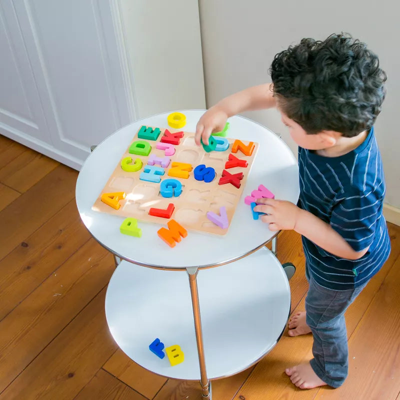 A young boy engaged in shape sorting with a New Classic Toys Alphabet Puzzle Uppercase on a table.