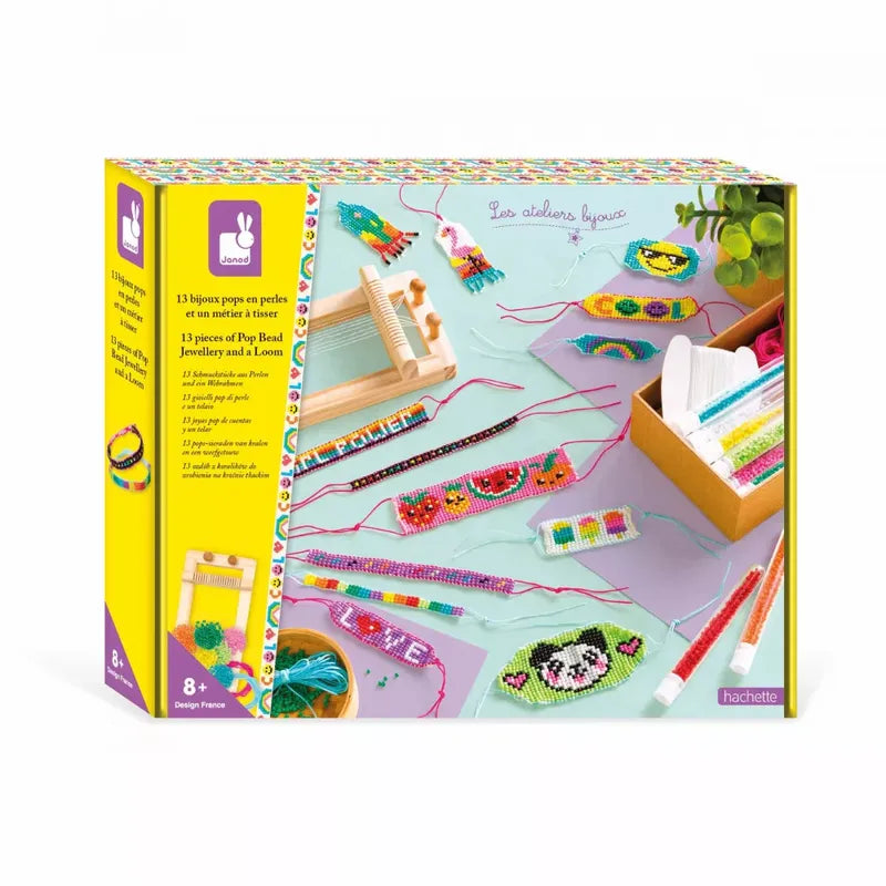 A colorful jewelry-making craft kit is shown, featuring various beaded designs such as bracelets and keychains arranged on a light blue surface. The box showcases several pieces and tools included, such as threads, beads, and crafting tools. The packaging is bright with playful illustrations. This is the Janod 13 Pieces Of Pop Bead Jewellery And Loom.