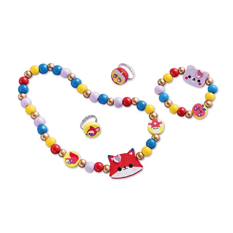 The Janod 4 Pieces Of Wooden Jewellery To Make Pretty Forest kit features a vibrant and colorful selection of children's jewelry, including a necklace with a red fox pendant, a bracelet adorned with a pink cow charm, and two rings featuring yellow and red designs. The wooden beads for kids come in an array of lively colors such as red, yellow, blue, purple, and metallic gold.