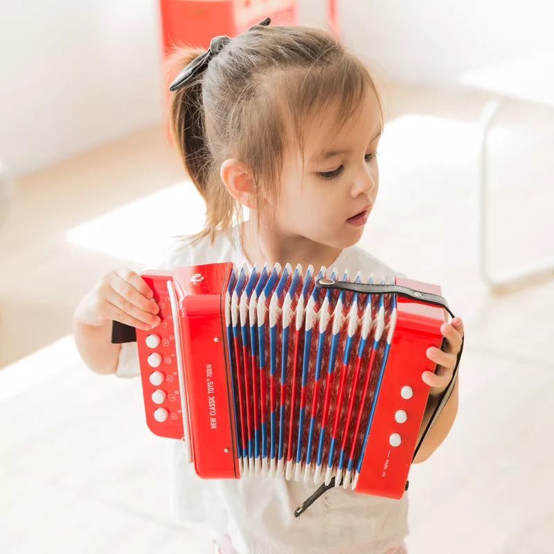 A little girl holding a New Classic Toys Red Accordion with Music Book.