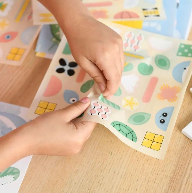 A person peels a colorful sticker from the Poppik Sticker Card Set Baby – Ocean, featuring fun shapes and ocean-themed designs on a light wooden surface—perfect for preschoolers to build fine motor skills through creative sticker play.