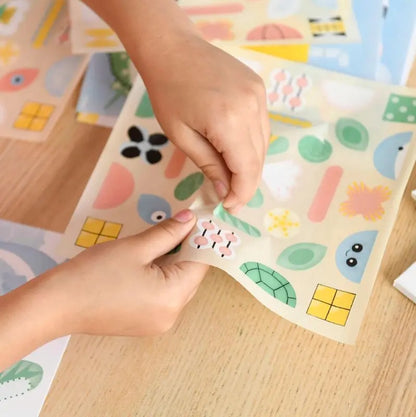 A person peels a colorful sticker from the Poppik Sticker Card Set Baby – Ocean, featuring fun shapes and ocean-themed designs on a light wooden surface—perfect for preschoolers to build fine motor skills through creative sticker play.