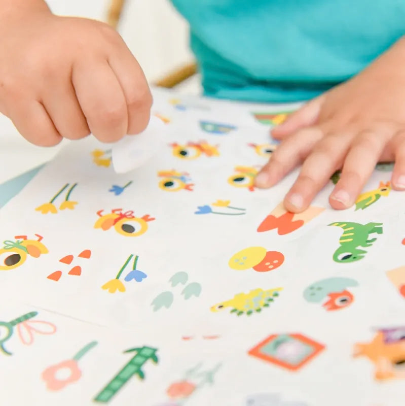 A child peels and places baby animal stickers from the Poppik Sticker Cards Set - Baby - Baby Animals on a white sheet, making preschool activities playful and fun.