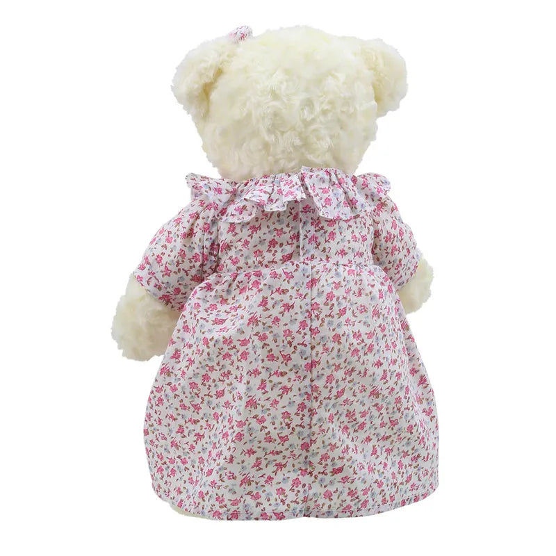 A fluffy white Wilberry Dressed Animal Bedtime Bear Nightie is shown from the back. This adorable bear toy is wearing a floral-patterned dress with pink and red flowers on a white background. The dress has a ruffled collar, and the bear has a matching bow on one ear, making it an ideal birthday present.