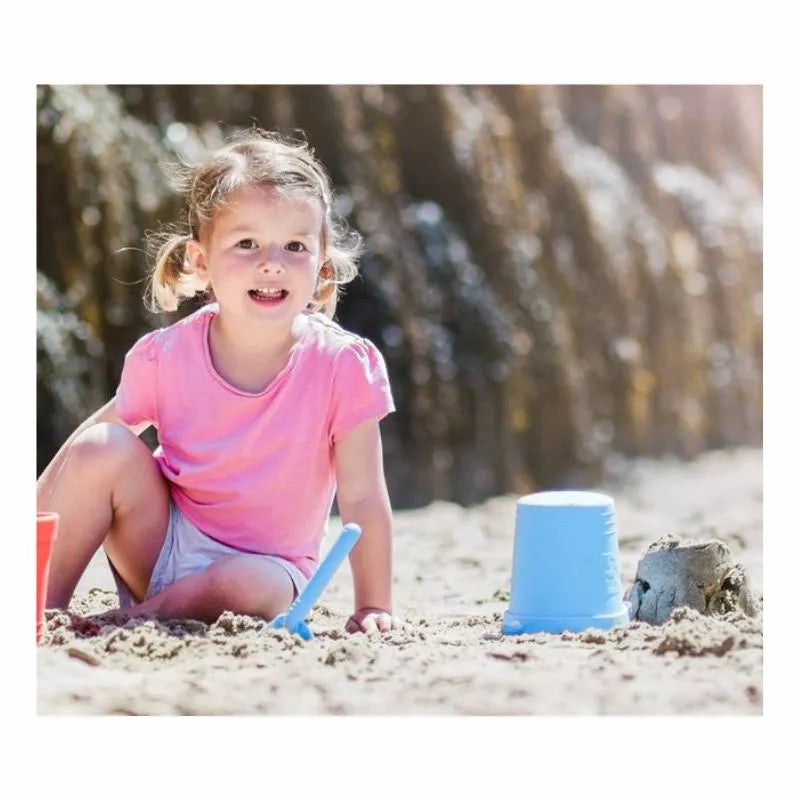 A little girl playing in the sand at the beach with her Powder Blue Eco Bucket & Spade.