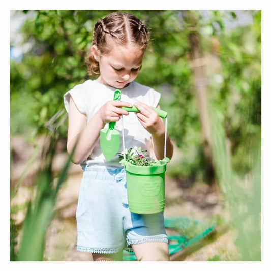 A little girl holding a Bigjigs Green Eco Bucket & Spade.