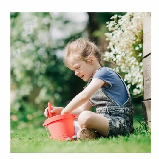 A young child playing with a Bigjigs Coral Pink Eco Bucket & Spade.