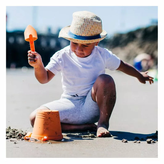 A little boy playing in the sand with a Bigjigs Apricot Eco Bucket & Spade.