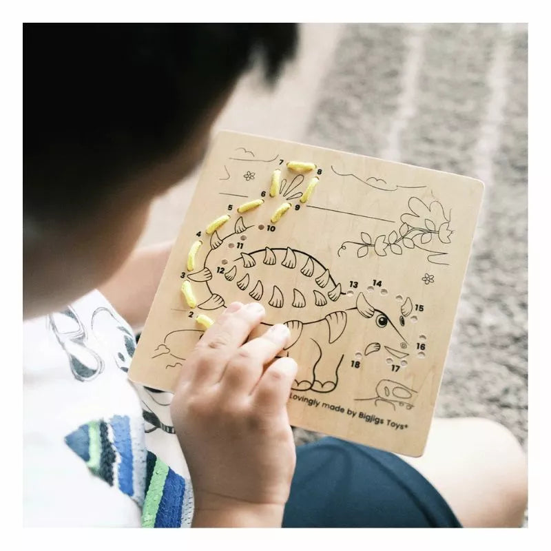 A child is drawing a picture of a Bigjigs Lacing by Numbers - Dinosaurs from the brand Bigjigs.