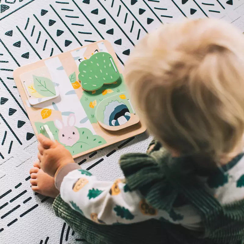 A toddler sitting on the floor playing with a Bigjigs Woodland Hide and Seek Puzzle.
