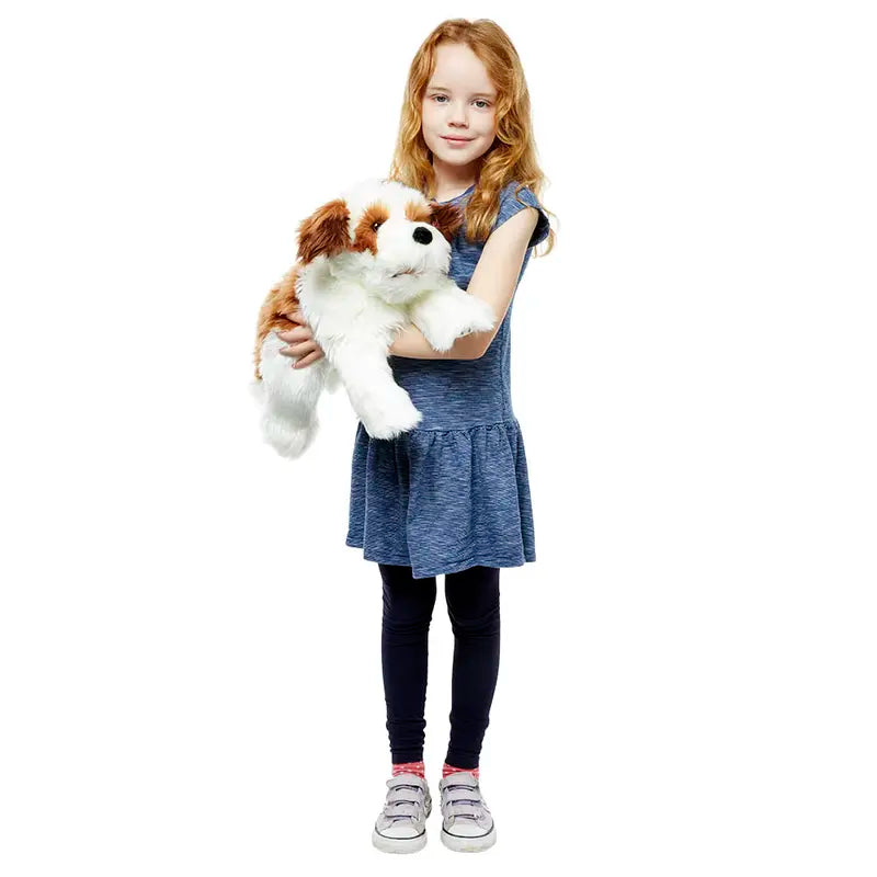 A young girl with long red hair, in a blue dress and black leggings, stands holding the Brown & White Hand Puppet - Playful Puppies against a white background.