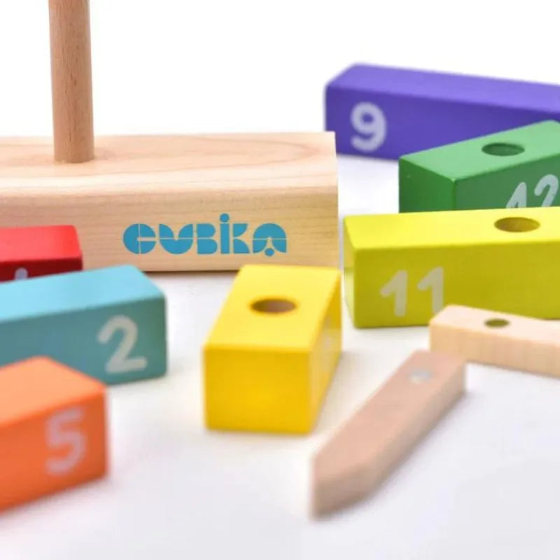 The Cubika ECO Wooden Construction Clock is an engaging developmental toy featuring a colorful assortment of wooden blocks with numbers, scattered around a wooden base with a vertical dowel. The blocks come in vibrant colors like yellow, green, purple, and blue, each showcasing a different number. The word "Ovika" is printed on the base.