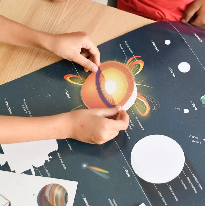 A child’s hands place a planet cross-section sticker onto the colorful Poppik Discovery Sticker Poster – Astronomy, which features illustrated planets and celestial objects.