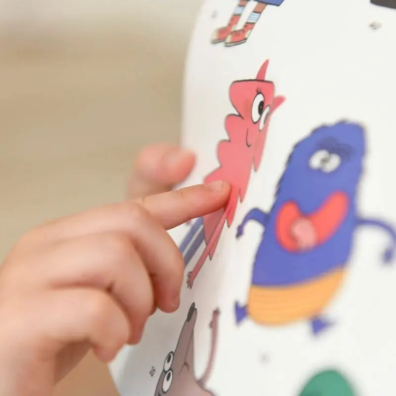 A child points at a pink cartoon character on the Poppik Discovery Sticker Poster – Emotion, an educational poster featuring colorful, whimsical monster illustrations.