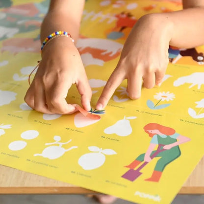 A child wearing a colorful beaded bracelet places a sticker on the Poppik Discovery Sticker Poster – Farm, a vibrant bilingual activity featuring fruits and gardening images, for an engaging and educational experience on a yellow background.