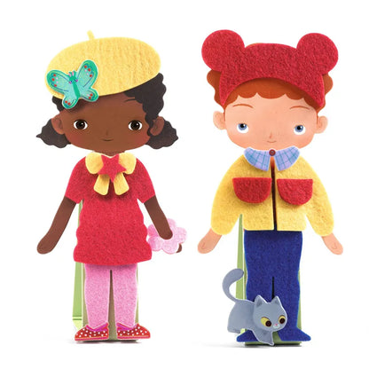 The Djeco Collages Soft dress-up dolls stand side by side in vibrant attire. The doll on the left sports a yellow beret adorned with a butterfly, paired with a red top and pink skirt. Meanwhile, the doll on the right showcases red hair under a matching red hat, along with a yellow jacket and blue pants. A small gray cat is positioned at their feet.