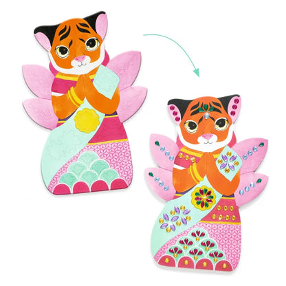 Illustration of a cute tiger cartoon character dressed in a vibrant and embellished outfit featuring intricate designs and sparkling gems, akin to the Djeco Stickers Rhinestones. The character has pink wings and is depicted in a praying pose, adorned with flower motifs. A curved arrow symbolizes a transformation evocative of a collage craft.