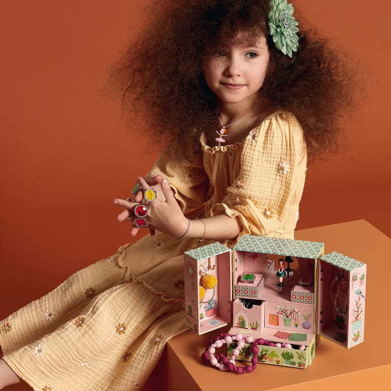 A little girl sitting on a table with a Djeco Music Box Secret Garden.