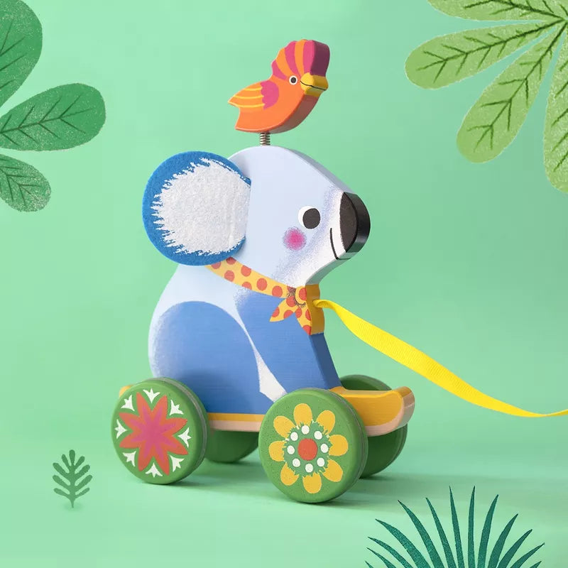 A Djeco Otto Pull along Toy koala bear riding a toy wagon with a bird on top of it.