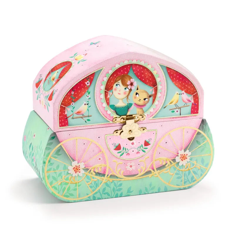 The Djeco Musical Box Carriage Ride is a colorful, whimsical jewellery box designed to look like a fairytale carriage. It features a girl and a cat in a window, ornate golden wheels, and vibrant illustrations of birds and flowers. The top half is pink, while the bottom half is green with floral details.