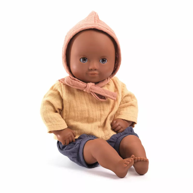 A Djeco Baby Mimosa Baby Doll sitting on the ground wearing a sweater and a hat.