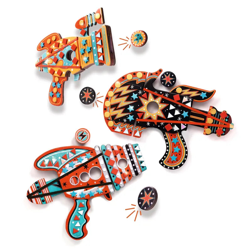 Three colorful, retro-styled Djeco Mosaics & Stickers Kosmik toy ray guns with vibrant geometric patterns and bold colors are displayed. The toy guns, resembling imaginative counter launchers, are arranged on a white background. Each one features various shapes, stars, and zigzag designs. Loose parts and mosaic stickers surround the guns.