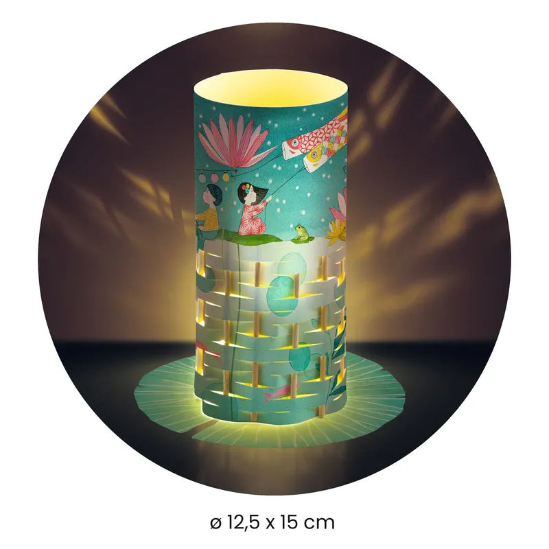 The Djeco Create Fireflies Dance is a cylindrical paper lantern featuring intricate cut-out designs and vibrant illustrations of flowers, a woman, and animals. It emits a warm glow that creates captivating patterns on the surrounding surfaces. The lantern measures 12.5 cm in diameter and 15 cm in height.