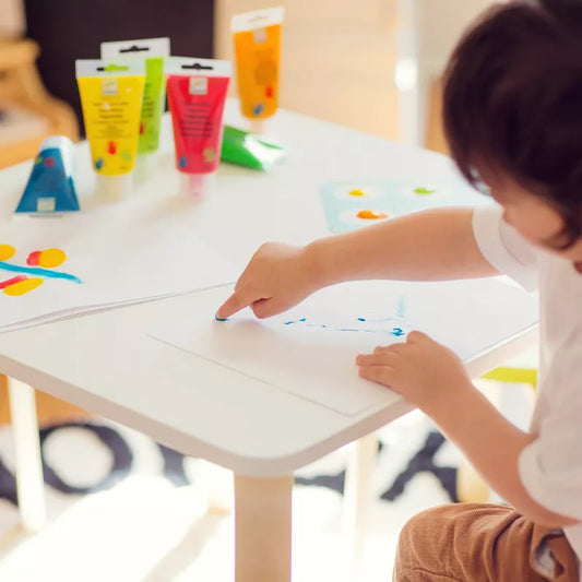 Little ones, budding artists, or children are using Djeco Paint For Little Ones 6 Finger Paint's Tubes to draw on a piece of paper at a table.