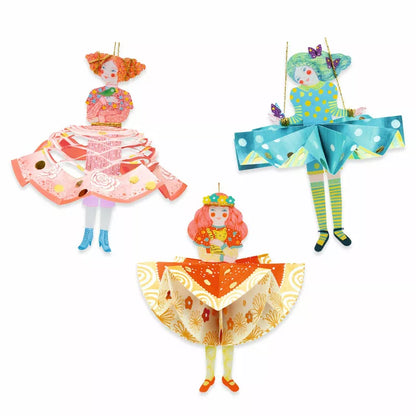 Three Djeco Paper Creations Paper Dresses with folding paper dresses hanging from a string on a white background.