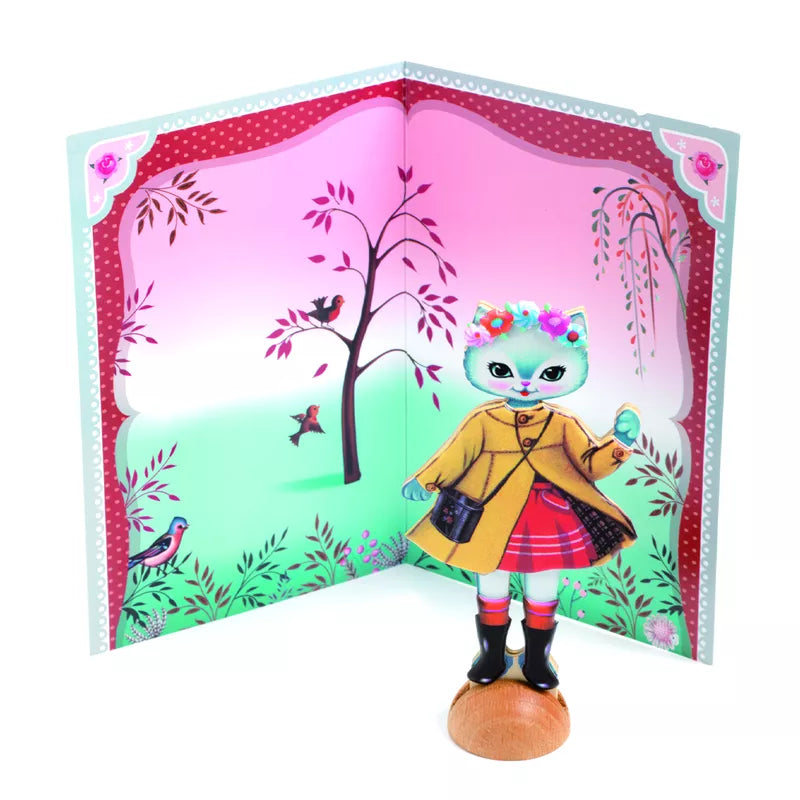 A wooden doll is standing in front of a card with a picture of a cat, engaging in Djeco Collage Little Wardrobe activity with keywords: toy.