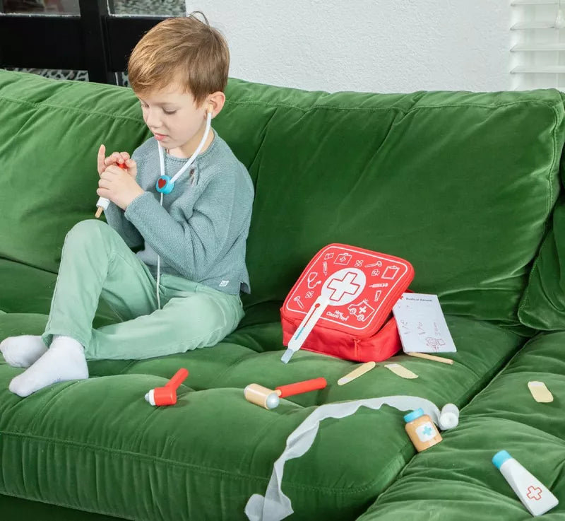 a young boy playing with the New Classic Toys Doctor Set on a green couch.