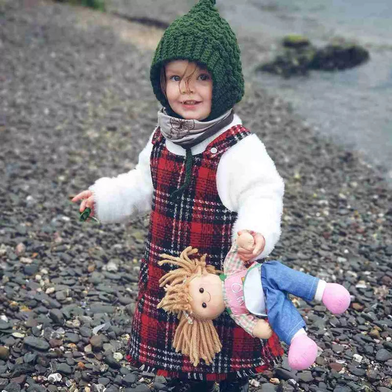 A little girl holding a Bigjigs Elsie Doll Medium on a rocky beach.