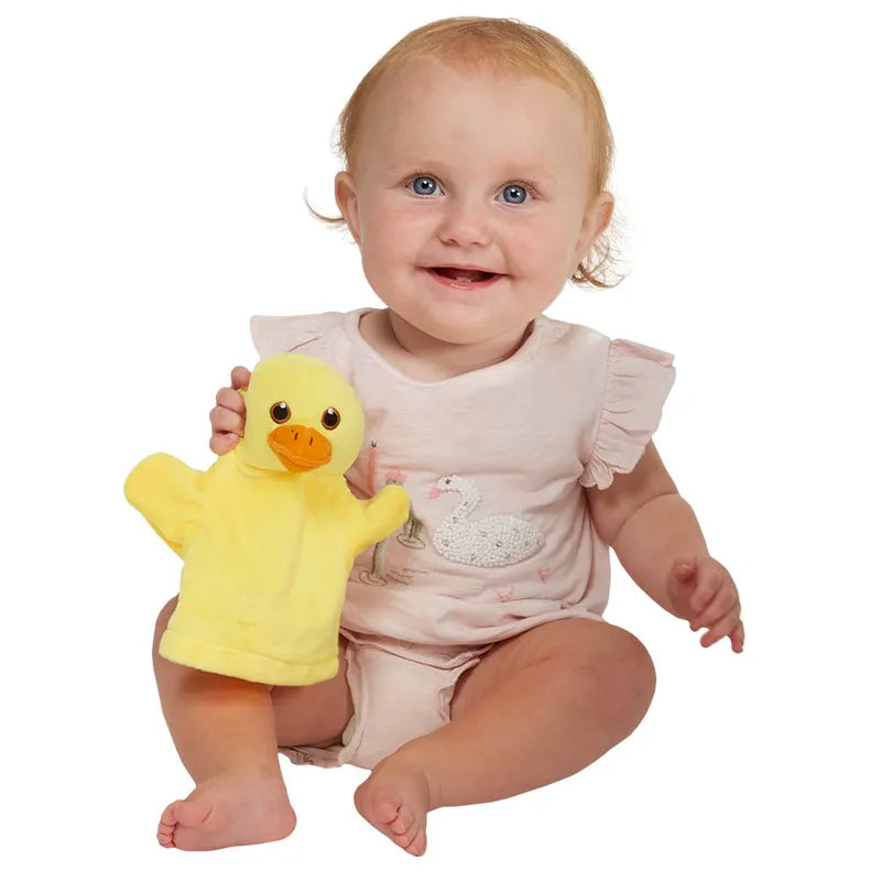 A smiling baby in a light pink outfit sits on the floor, holding **The Puppet Company My First Puppet Duck**, a yellow hand puppet with an orange beak and feet. This playful moment not only captivates their blue eyes and light brown hair but also aids in developing early communication skills against the plain white background.