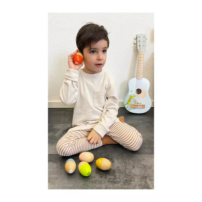A young boy sitting on the floor holding Musical Eggs "Groovy Beats".