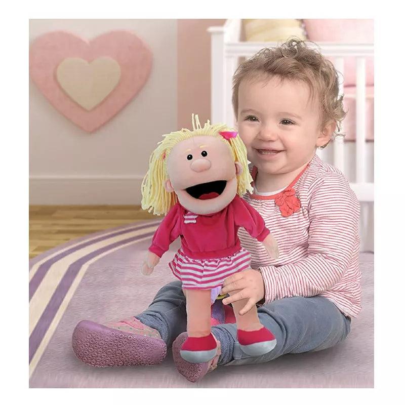 A Fiesta Crafts girl mouth moving hand puppet sitting on the floor holding a stuffed animal.