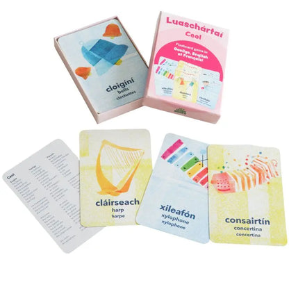 A pink box labeled "Luaschártaí - Ceol" contains trilingual music flashcards with illustrations and names of instruments—like harp, xylophone, and concertina—in Irish, English, and a third language.