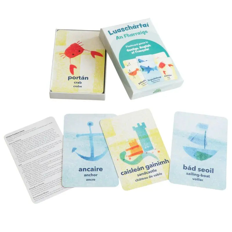 Luaschártaí - An Fharraige is a set of illustrated trilingual flashcards with sea-themed words in Irish, English, and French. Visible cards include a crab, anchor, sandcastle, and sailing boat—ideal for Irish language learners.